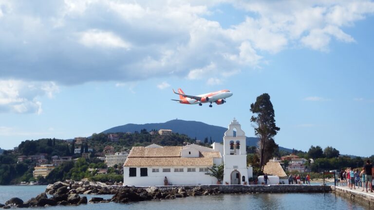 Airplane flying over a white monastery by the sea.