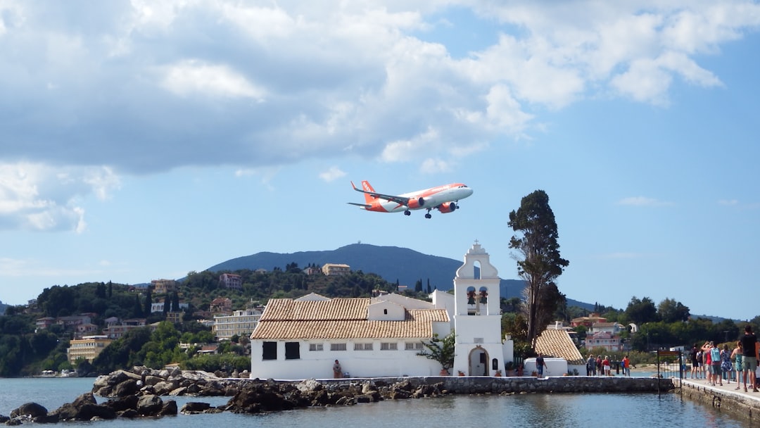 Airplane flying over a white monastery by the sea.