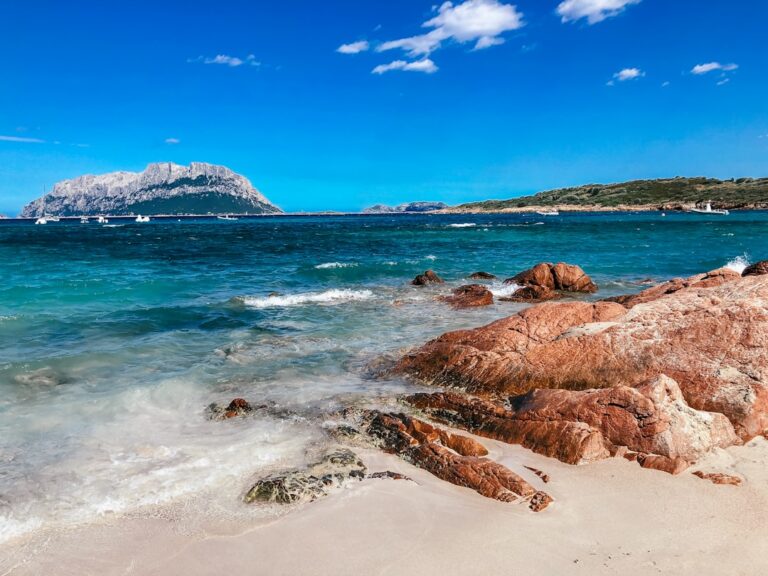 a rocky beach with clear blue water and a mountain in the distance