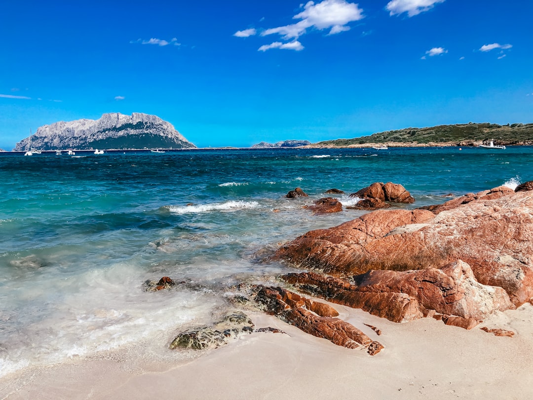 a rocky beach with clear blue water and a mountain in the distance