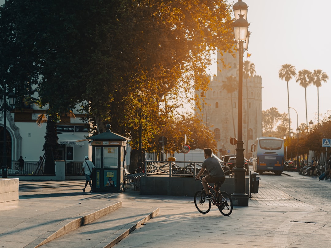 Man cycles down sunny street past old building.